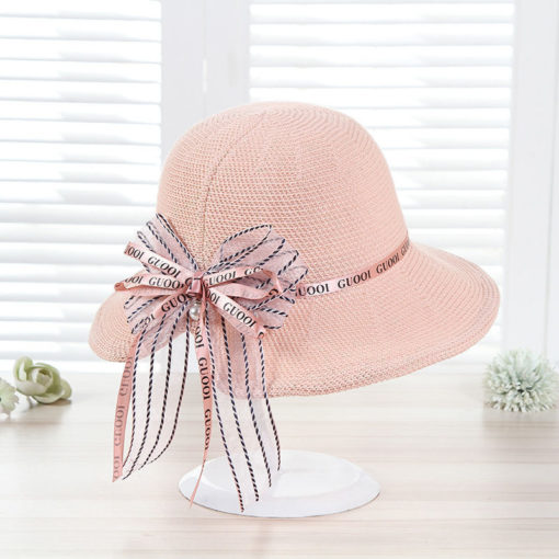 Pink straw sun hat with an elegant "GUOOI" ribbon bow, displayed on a table, ideal for stylish summer outings.