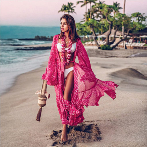 Woman wearing a rose red bohemian polka dot beach cover-up with flared sleeves, walking along the beach for a chic seaside look.